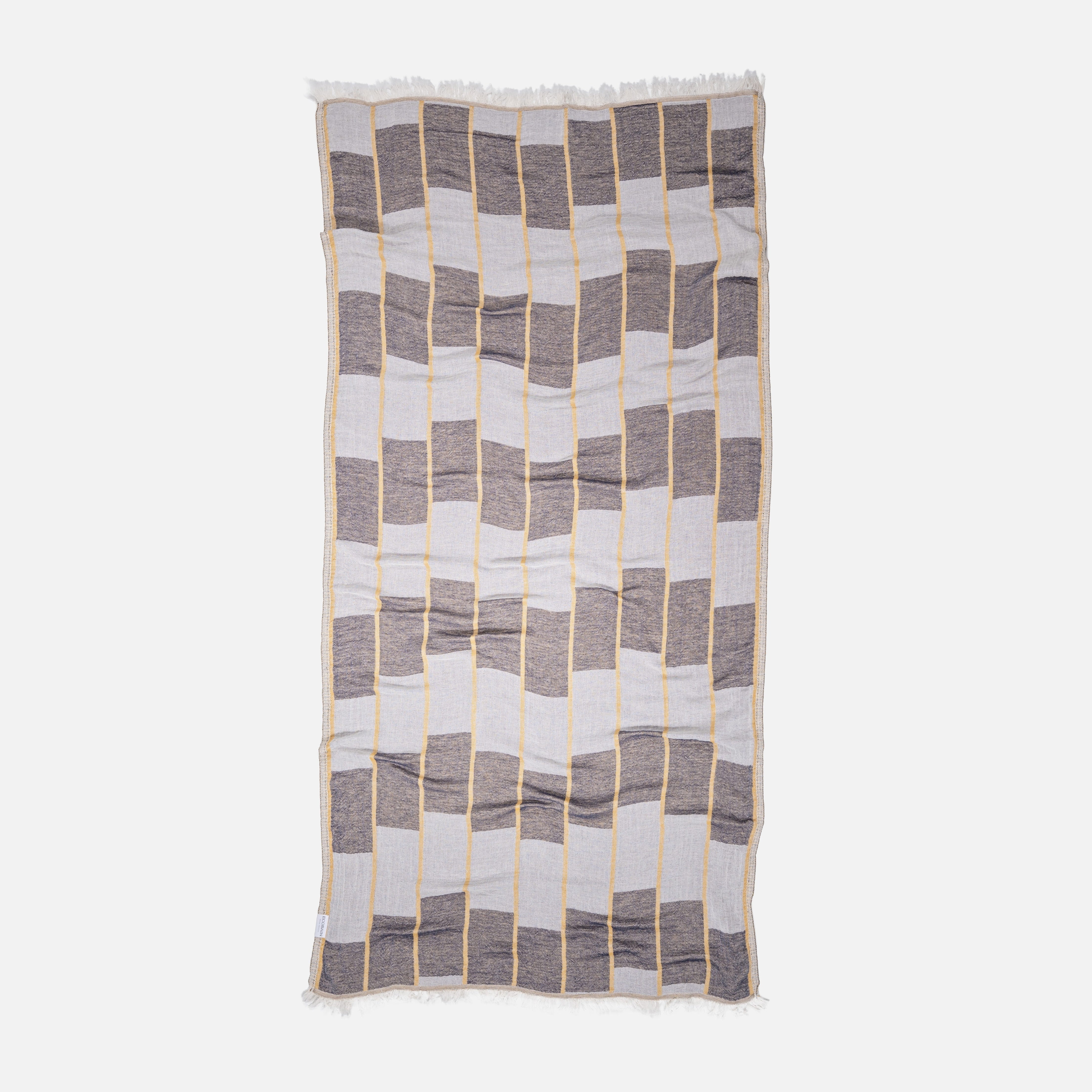 Detailaufnahme der gewebten Karostruktur des Ecobain Premiumtuchs 'Chess' in der Nuance Mustard Seed. Das schnelltrocknende, weiche Baumwolltuch ist der perfekte, platzsparende Begleiter für den nächsten Segeltörn, Wellness-Urlaub oder im minimalistischen Reise-Handgepäck – ein klares Statement für moderne Badekultur.