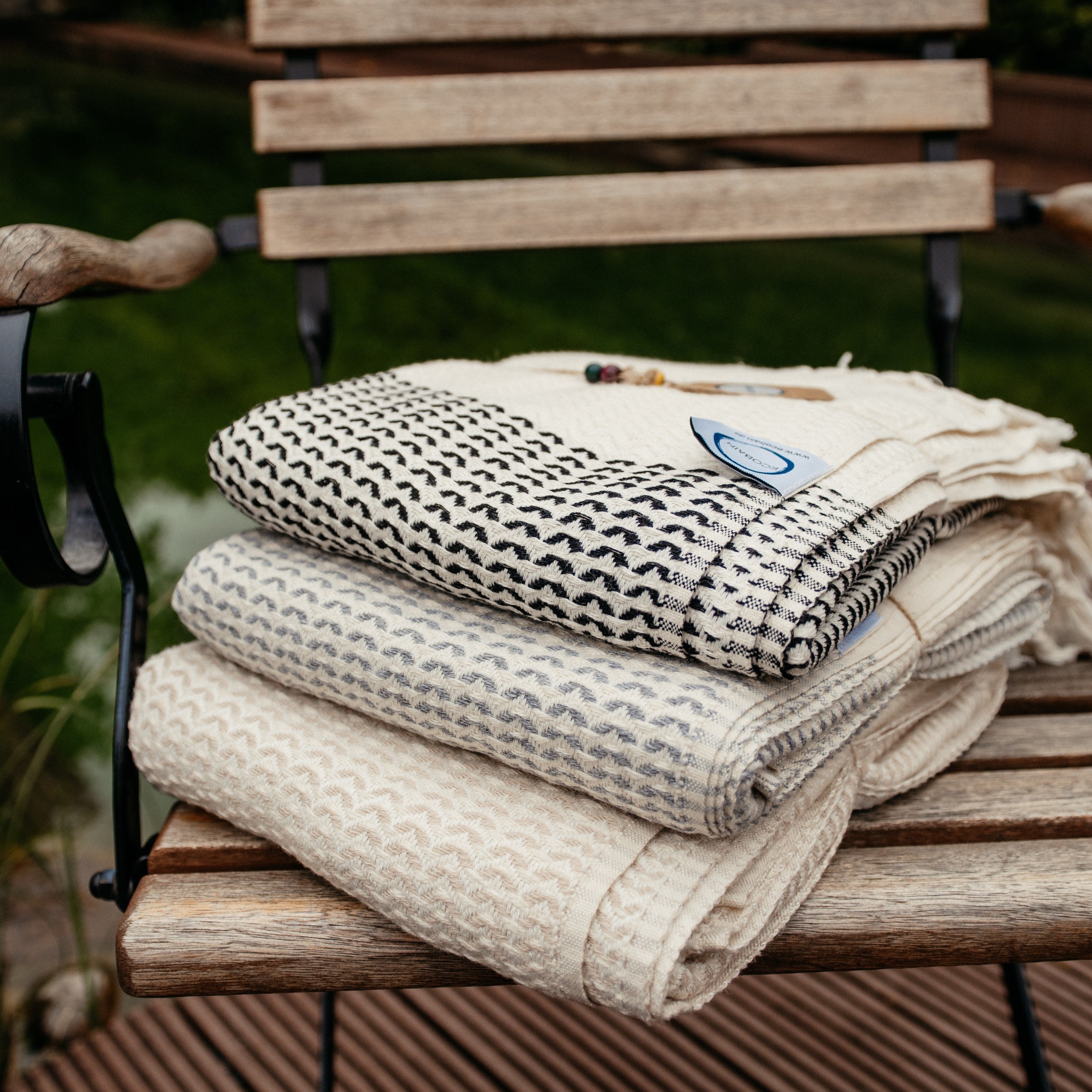 Stapel aus weichen Ecobain Gordion Towels in verschiedenen Grautönen auf einem hellen Holzregal.