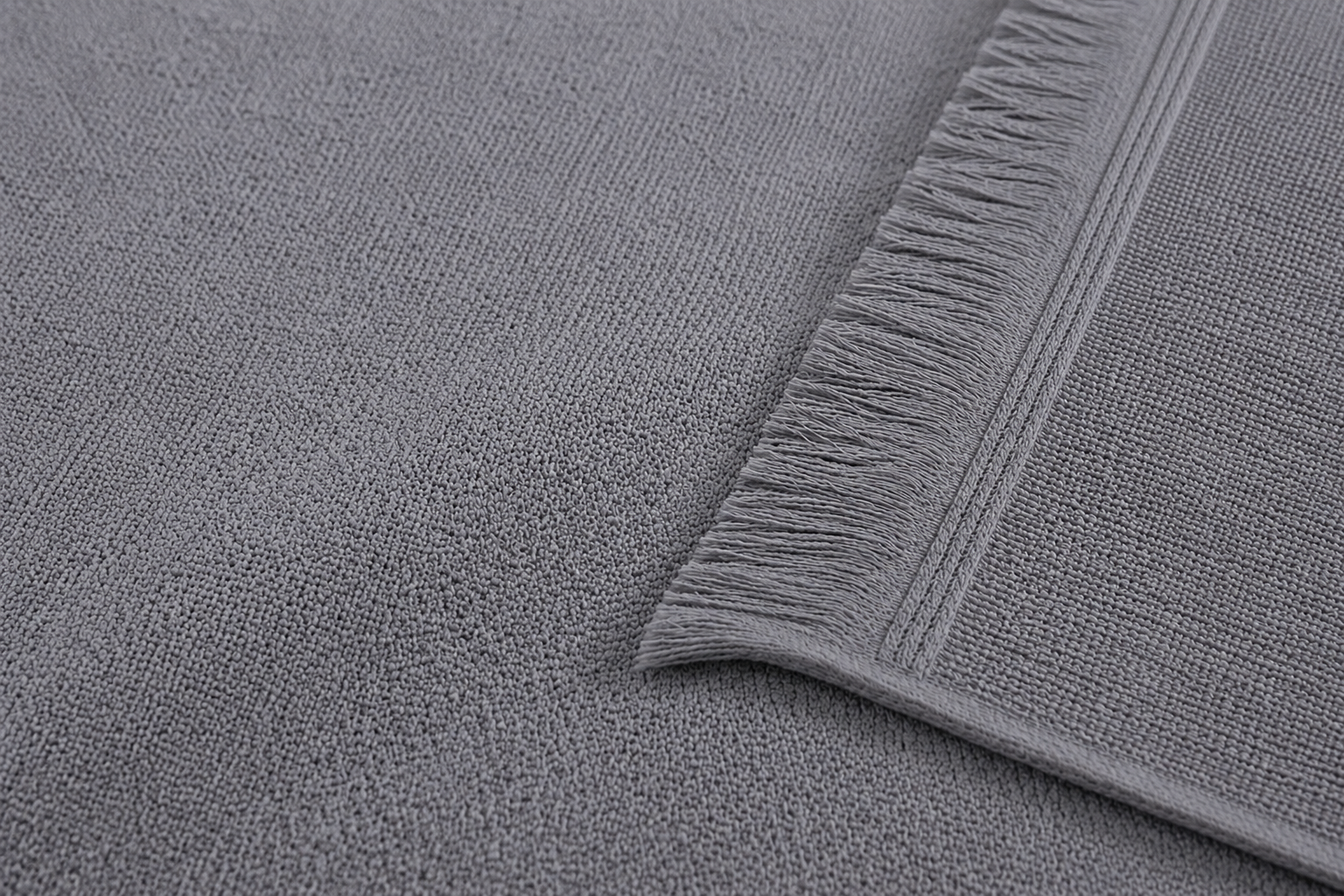 Detaillierte Nahaufnahme des Ecobain Hybrid Handtuchs in Storm Cloud Grau. Die Aufnahme zeigt die komplexe, kontrastierende Webstruktur: Eine glatte, feinere Gewebefläche grenzt direkt an eine dichtere, Jacquard-ähnliche Textur. Die precision-stitched Kante mit dem integrierten, weichen Fransenbesatz ist klar und scharf fokussiert.
