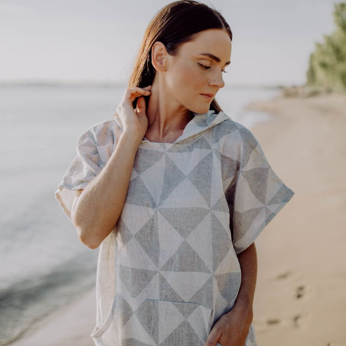 Rückansicht einer Person, die den atmungsaktiven Ecobain Poncho Symique in Mountain Grey im Freien trägt, Fokus auf den weichen Fall des Stoffes.