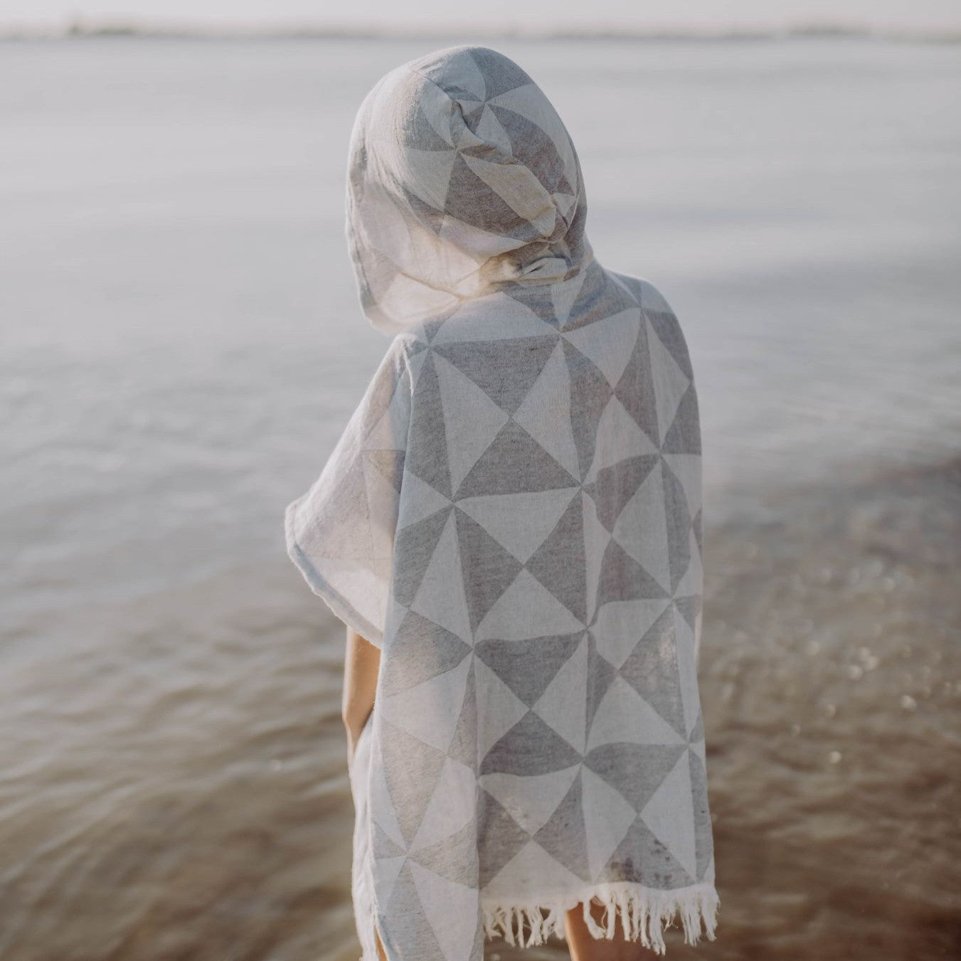Eine Person trägt den saugstarken Ecobain Poncho Symique in Mountain Grey, ideal als wärmender und schützender Überwurf nach dem Schwimmen.