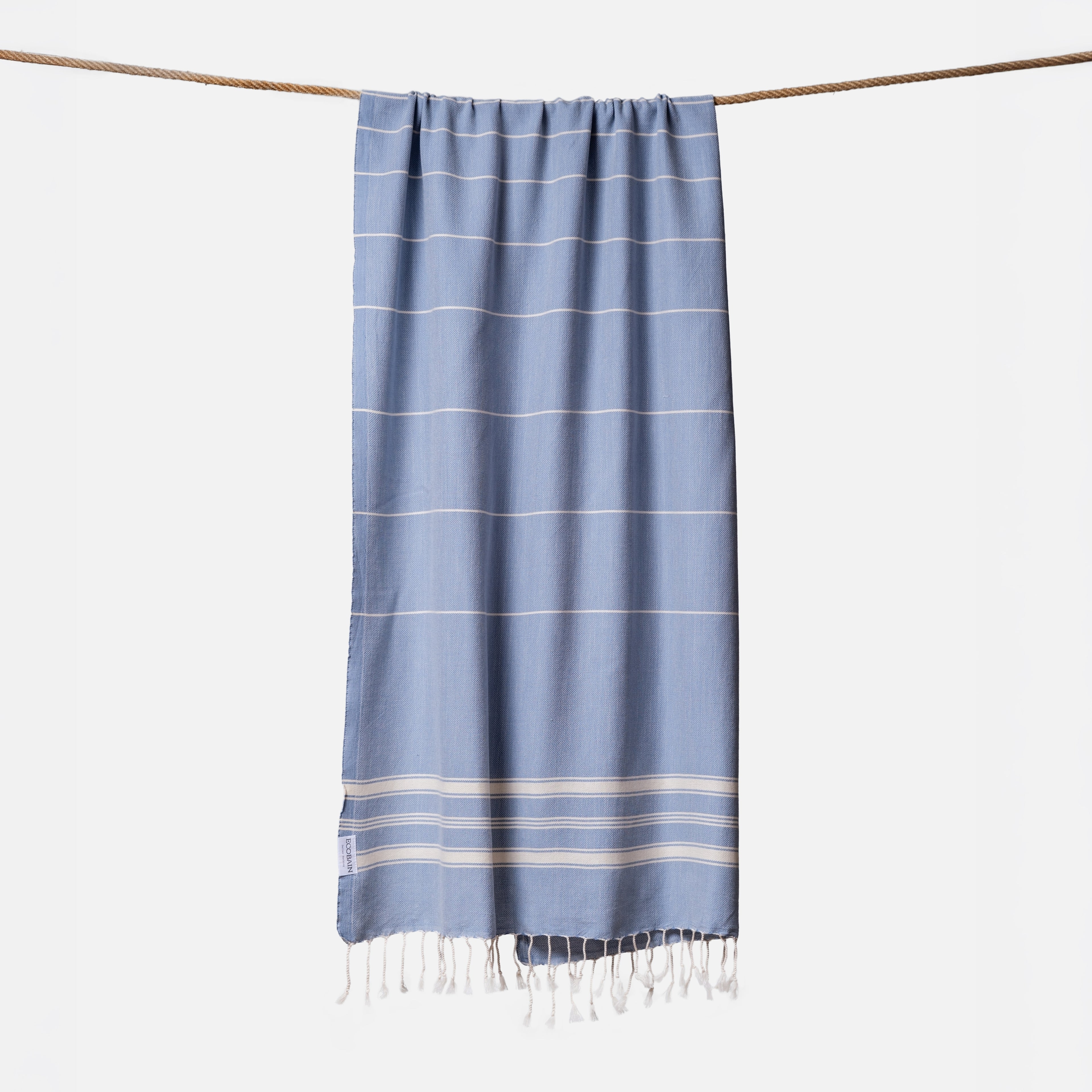 Extragroßes Ecobain Strandtuch der Liberty Series im tiefen Ozeanton Deep Tide. Das platzsparende Pestemal in 100x200 cm wird stilvoll gerollt mit originalem Hang Tag geliefert und ist die ideale nachhaltige Geschenkidee für Segler und Vanlife-Fans. Ein komplett sandfreies Reisehandtuch aus pestizidfreiem Anbau, das mit seiner extremen Saugkraft herkömmliche Frottee-Saunatücher bei jedem Outdoor-Abenteuer alt aussehen lässt.