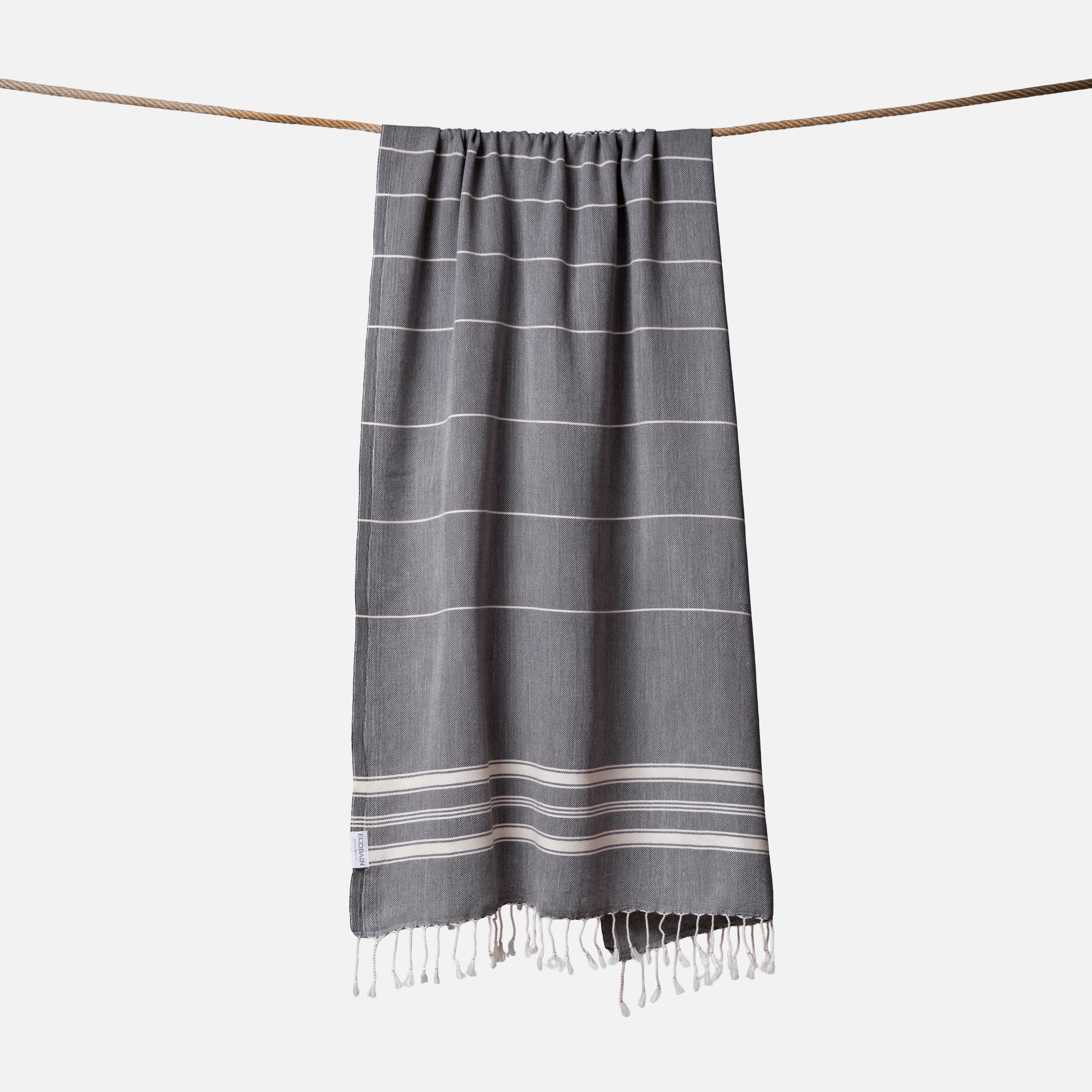 Extragroßes Ecobain Strandlaken der Liberty Series im kraftvollen Anthrazit Storm Cloud. Das platzsparende Pestemal in 100x200 cm wird stilvoll gerollt mit originalem Hang Tag geliefert und ist die ideale nachhaltige Geschenkidee für Outdoor-Fans und Saunagänger. Ein absolut sandfreies Reisehandtuch aus pestizidfreiem Anbau, das bei jedem Ausflug die Badetasche federleicht hält und herkömmliches Frottee ersetzt.