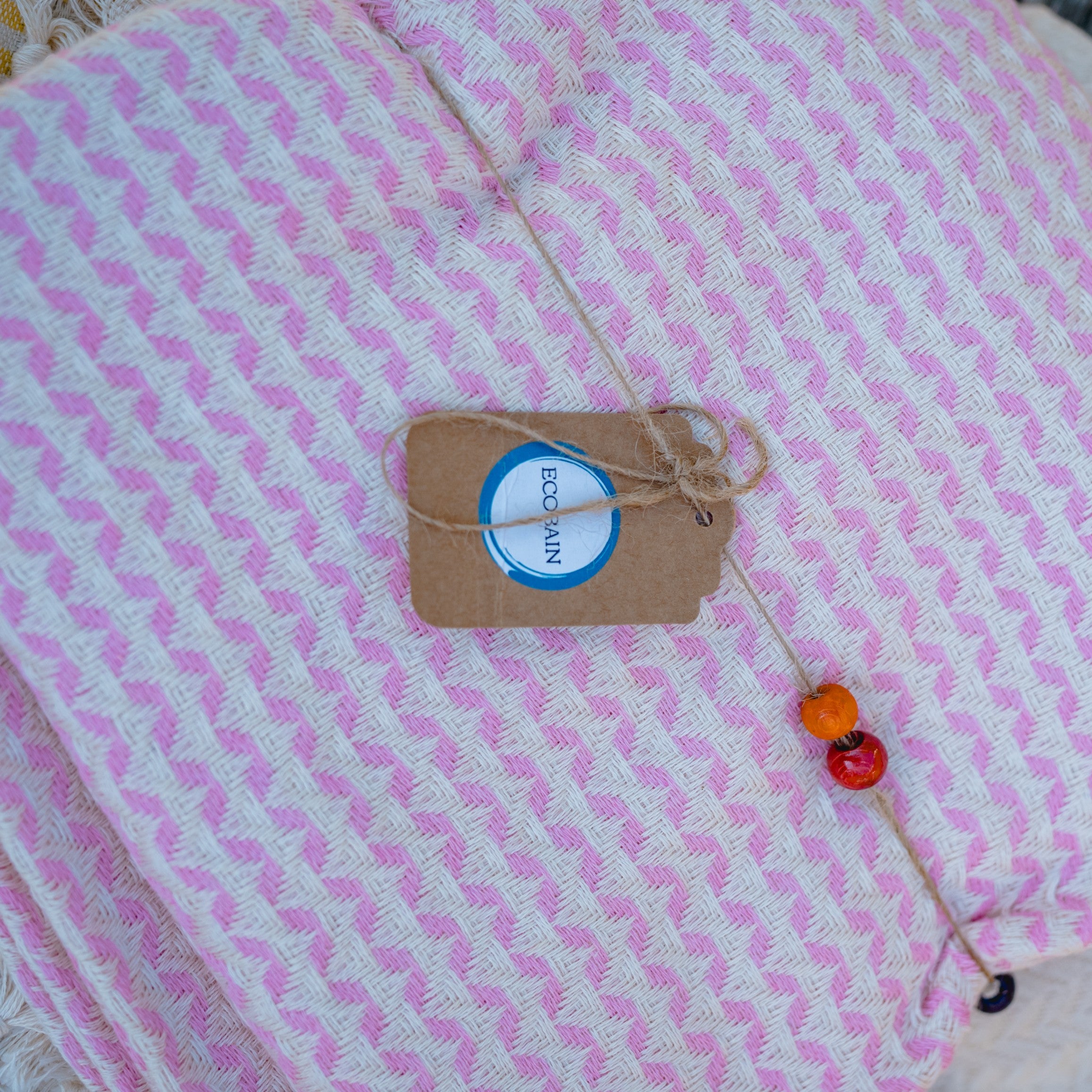 Ein an einer weißen Wand hängendes Ecobain Gordion Towel in sanftem Rosa (Soft Pink), das das feine Webmuster und die handgeknüpften Fransen am unteren Ende zeigt.